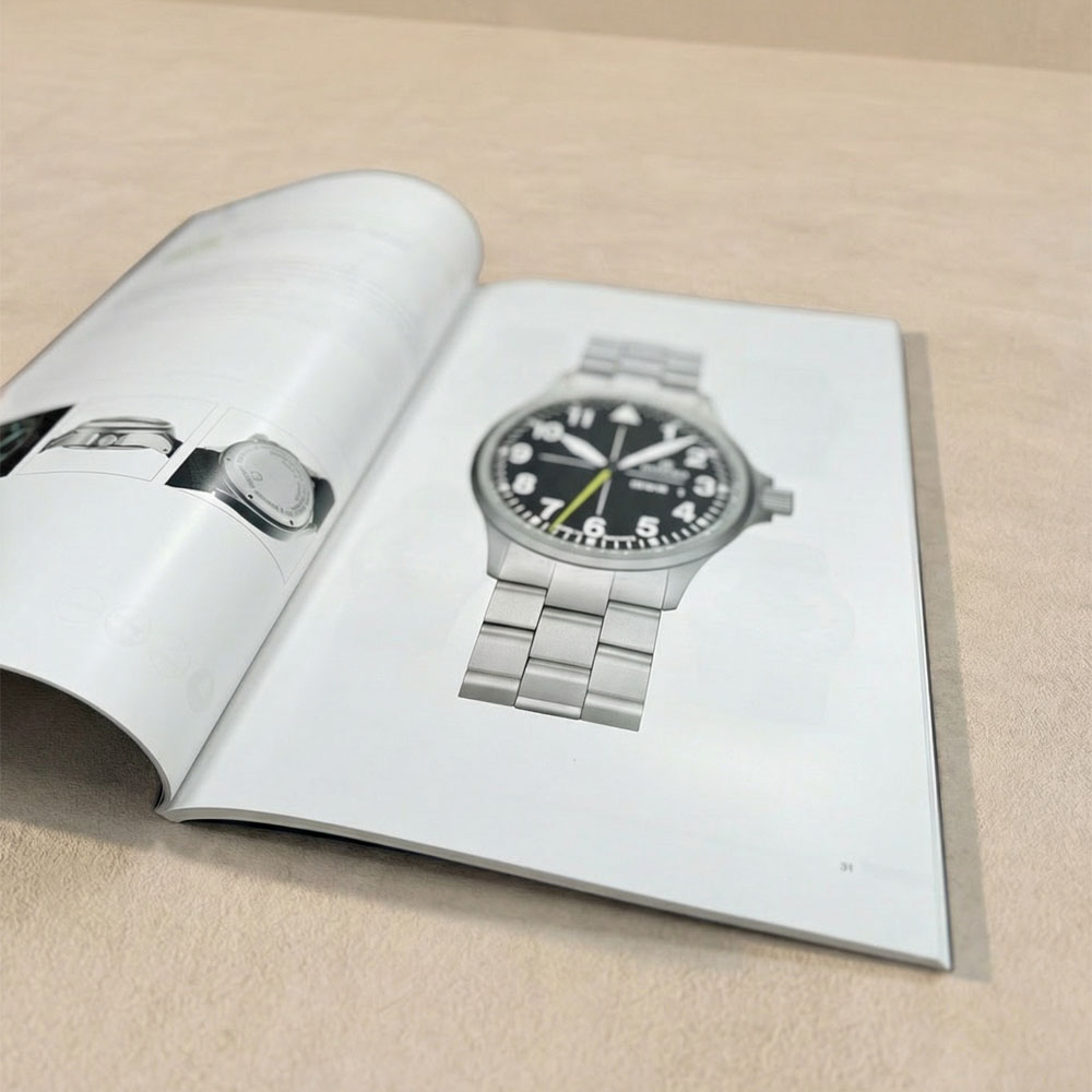 Ein offenes Magazin mit einer Abbildung von eienr hochwertigen Uhr in grau liegt auf einem beigen Untergrund